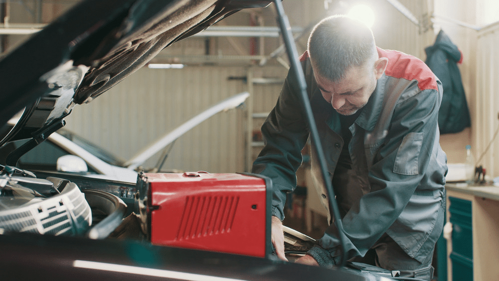 image Mechanic working under a car hood in a garage, checking engine with tools and equipment nearby. | Sky Rye Design Mechanic working under a car hood in a garage, checking engine with tools and equipment nearby.