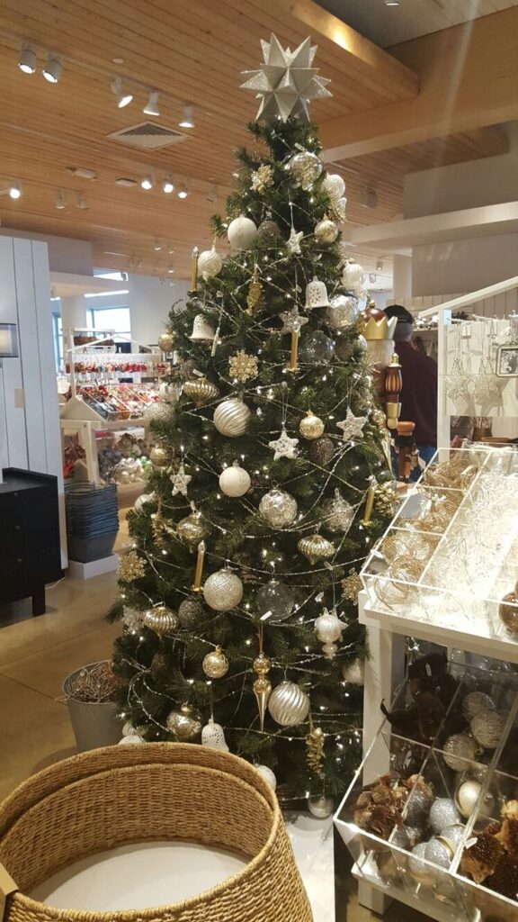 A beautifully decorated Christmas tree with gold and silver ornaments, inside a festive store, surrounded by holiday decorations.