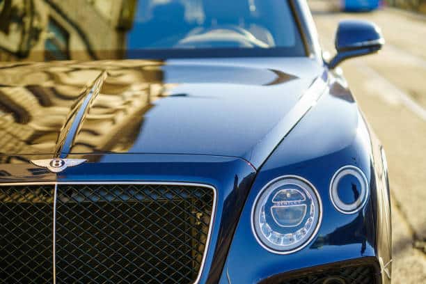 Luxurious blue car with detailed front grille and headlight design, parked on a sunlit city street.
