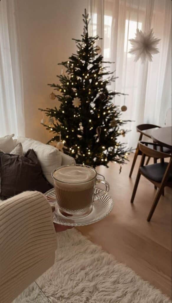 Cozy living room with decorated Christmas tree and a cup of coffee on a saucer being held in the foreground.