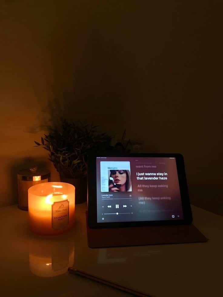 Cozy scene with a lit candle and tablet displaying music lyrics on a dimly lit desk, creating a relaxing atmosphere.