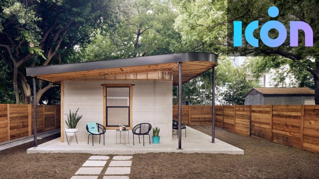 3D-printed tiny home by ICON, surrounded by trees and wooden fence, featuring a modern porch with seating.
