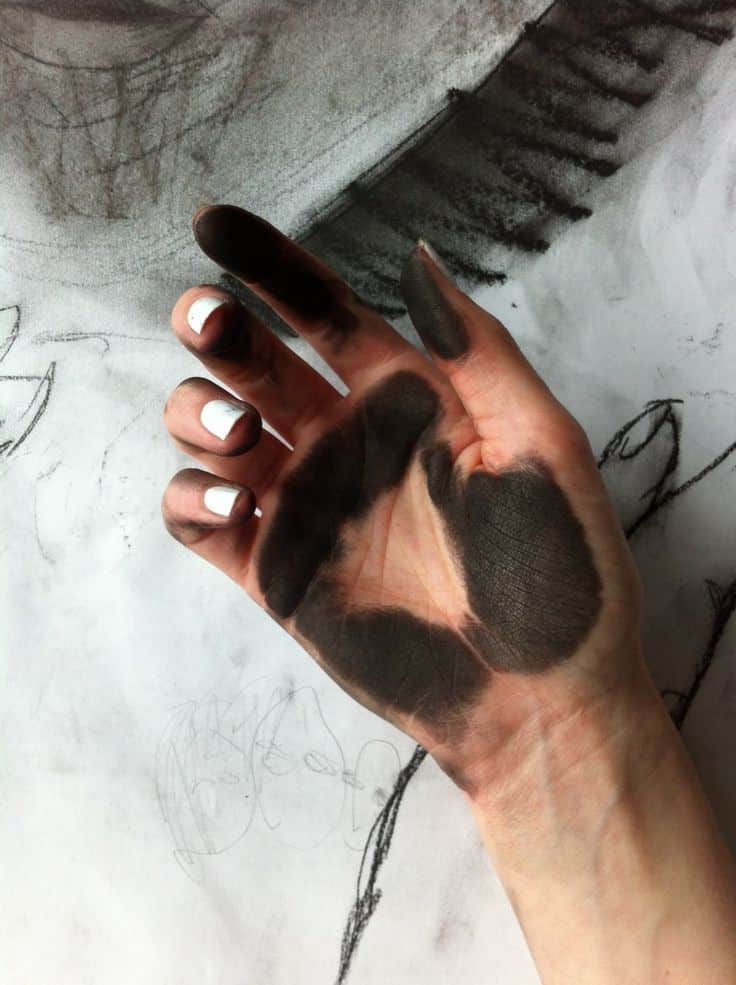 Artist's hand with charcoal stains over sketch paper, highlighting creative process and art techniques in drawing.