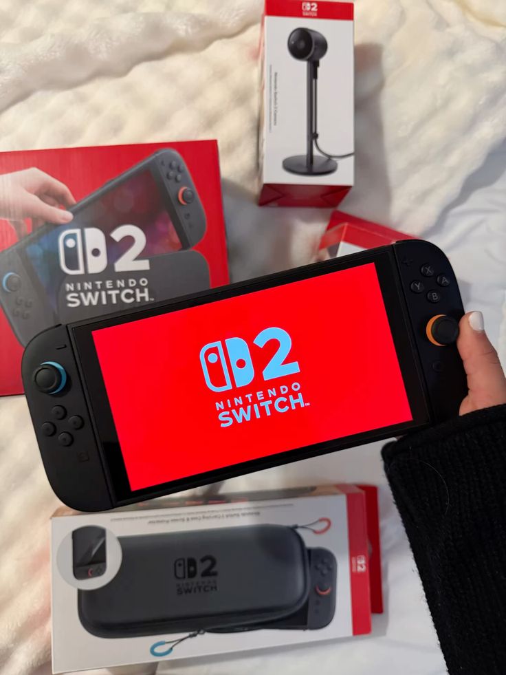 Hand holding a Nintendo Switch D2 with accessories on a bed, showcasing the gaming console and packaging.