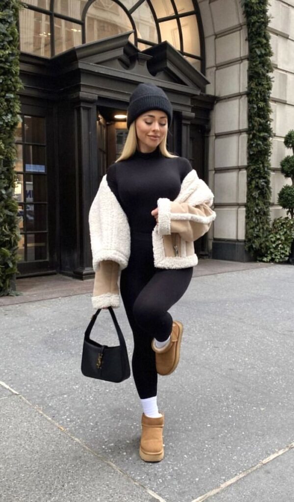 Woman in stylish winter outfit, wearing a beanie and boots, poses confidently outdoors on a city sidewalk.