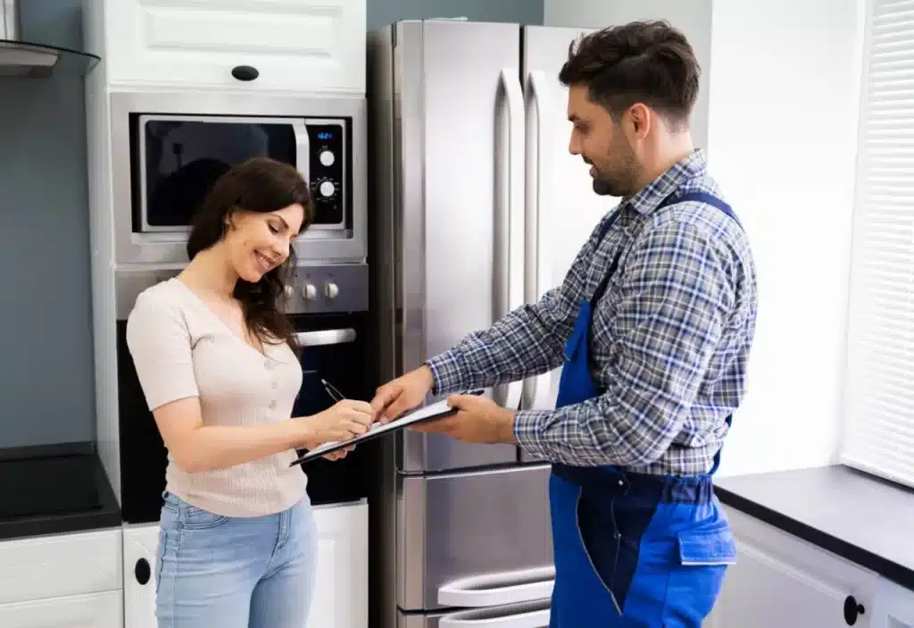 Woman signing a document for an appliance repairman in a kitchen.
