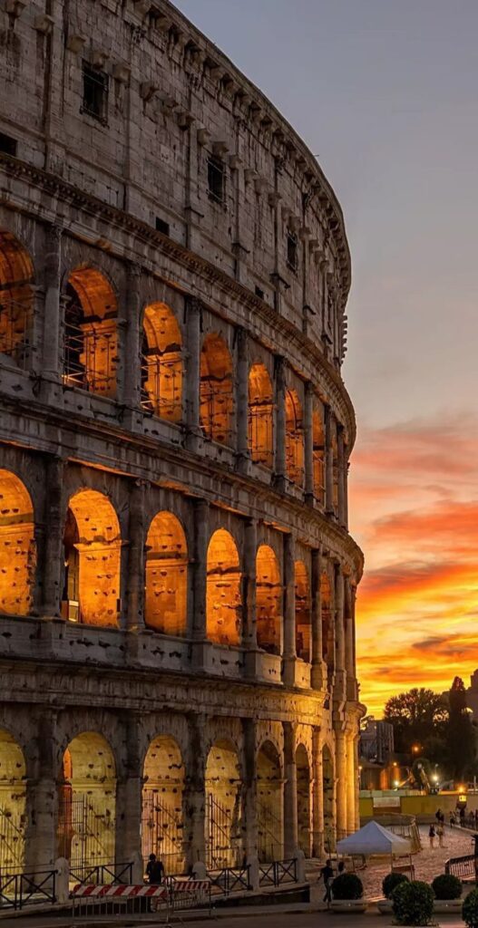 ratgbhe The Colosseum at sunset with illuminated arches, Rome, showcasing its ancient architectural grandeur. | Sky Rye Design The Colosseum at sunset with illuminated arches, Rome, showcasing its ancient architectural grandeur.