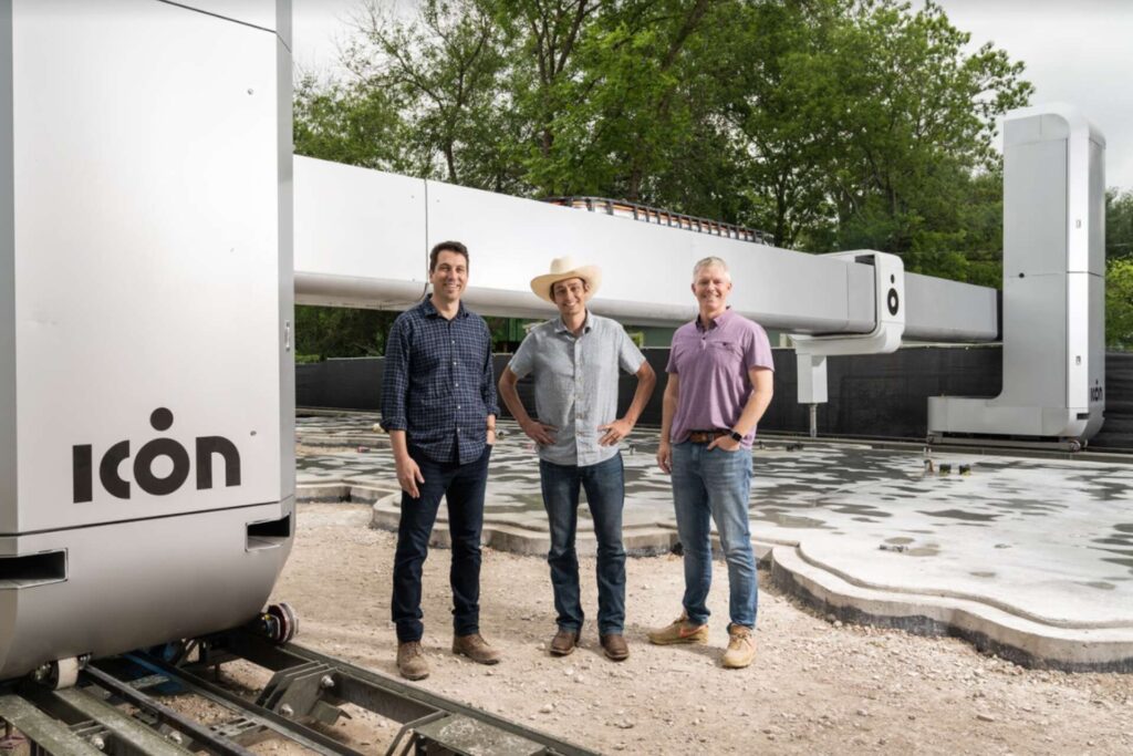 ratio3x2_1920 Three men standing in front of Icon 3D printing construction machine at a building site. | Sky Rye Design Three men standing in front of Icon 3D printing construction machine at a building site.