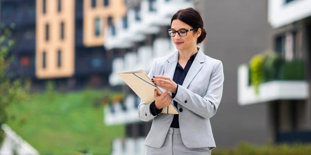 Businesswoman in a gray suit taking notes outdoors in an urban setting, representing professional success and real estate management.