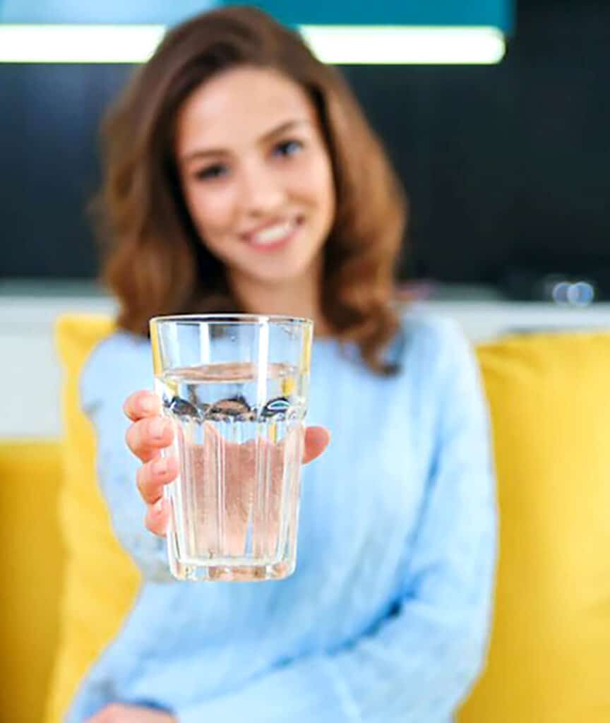 review-1 Woman offering a glass of water, promoting hydration and healthy lifestyle in a cozy, modern setting. | Sky Rye Design Woman offering a glass of water, promoting hydration and healthy lifestyle in a cozy, modern setting.