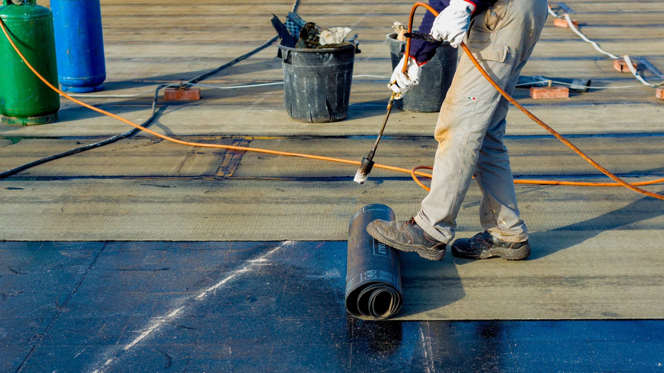 Technician applying waterproofing membrane with a torch on a flat roof. Roofing tools and materials are visible, ensuring protection.