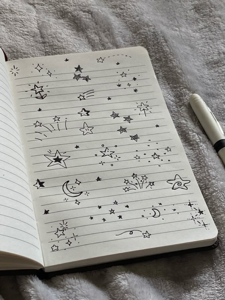 Notebook with star and moon doodles on lined pages, displayed on a cozy, textured surface, next to a black and white pen.