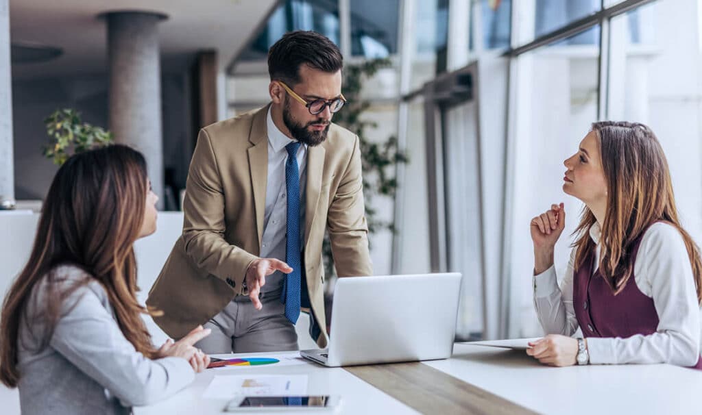 Business meeting in modern office with three professionals discussing work around a laptop, focused on collaboration and strategy.