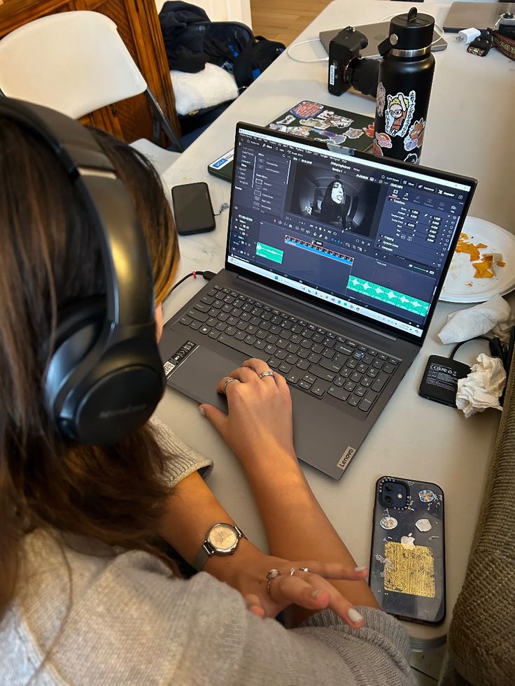 time to edit Person editing video on laptop with headphones at cluttered desk. | Sky Rye Design Person editing video on laptop with headphones at cluttered desk.