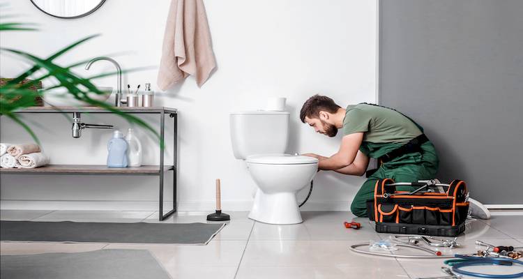 Plumber fixing a toilet in modern bathroom, surrounded by tools and supplies. Home repair and maintenance concept.