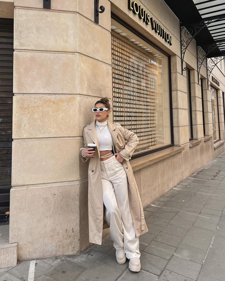 Fashionable woman in beige trench coat with coffee outside a Louis Vuitton store.