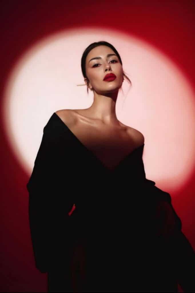 Elegant woman in black dress with red lipstick, dramatic lighting against a red background. Fashion portrait photography.