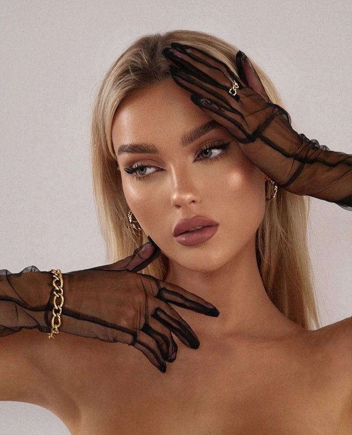 Woman with long blonde hair wearing sheer black gloves and gold accessories striking a pose.