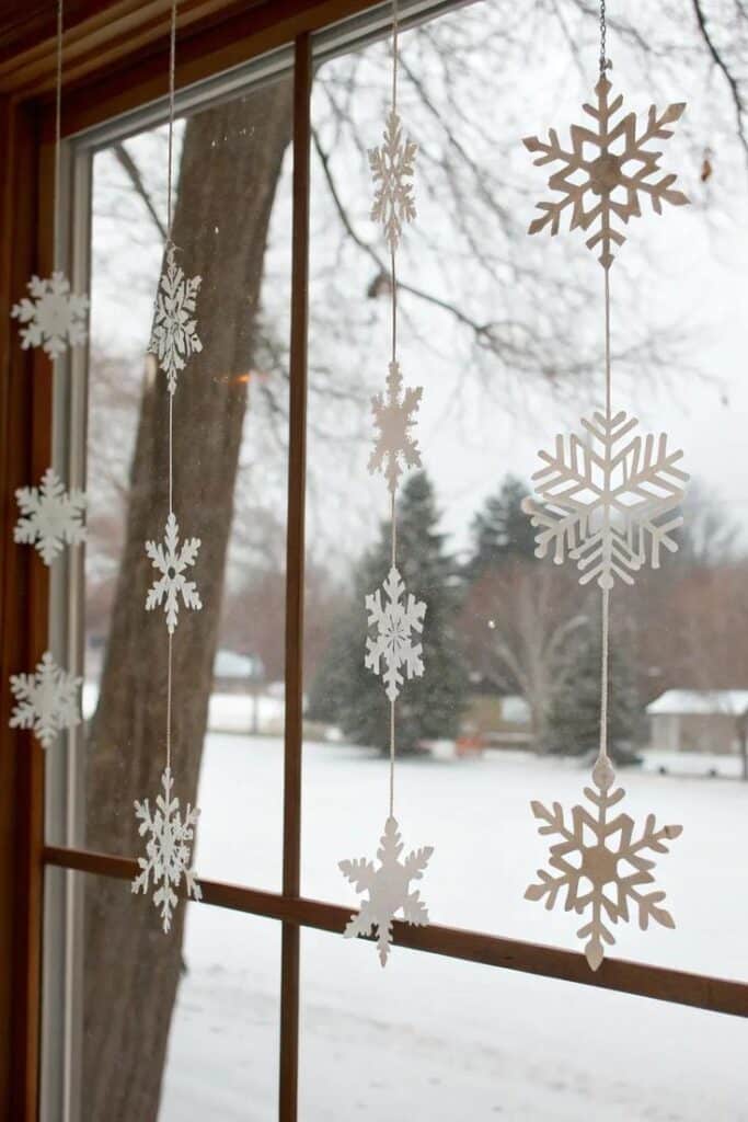 undefined 67 Paper snowflakes hanging on a window with a snowy outdoor view, capturing the essence of winter decor. | Sky Rye Design Paper snowflakes hanging on a window with a snowy outdoor view, capturing the essence of winter decor.