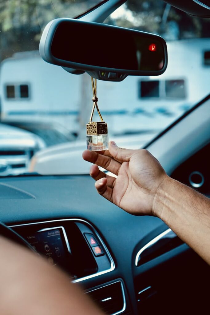 Hand adjusting a hanging car air freshener inside a vehicle for a pleasant fragrance.