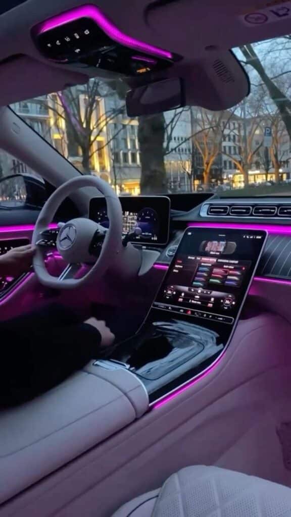 Luxurious car interior with ambient pink LED lighting, modern dashboard, and touchscreen display featuring various controls.