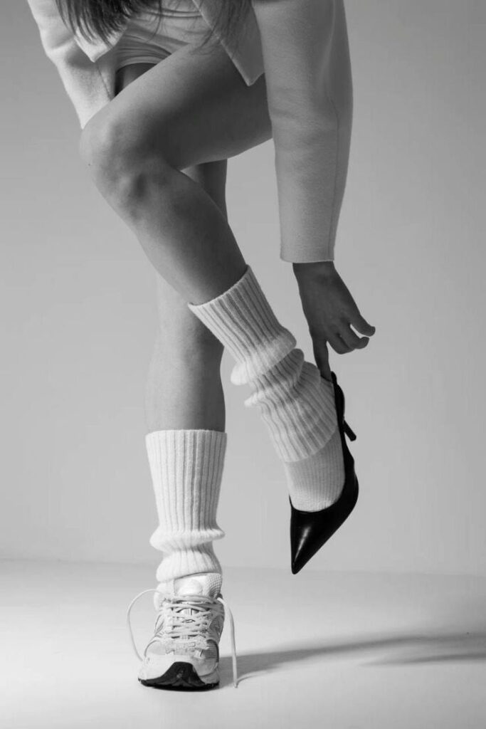 Woman wearing one sneaker and one high heel, showcasing a contrast in footwear and fashion styles.