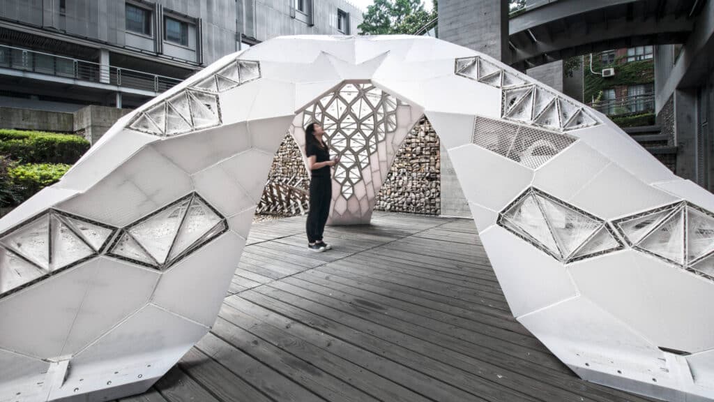 Innovative geometric pavilion with a visitor inside, featuring interlocking triangular panels and modern architectural design.