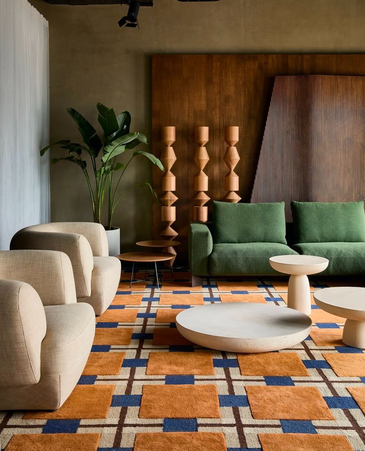 Modern living room with green couches, beige chairs, geometric rug, and decorative wooden elements. Contemporary design and stylish decor.
