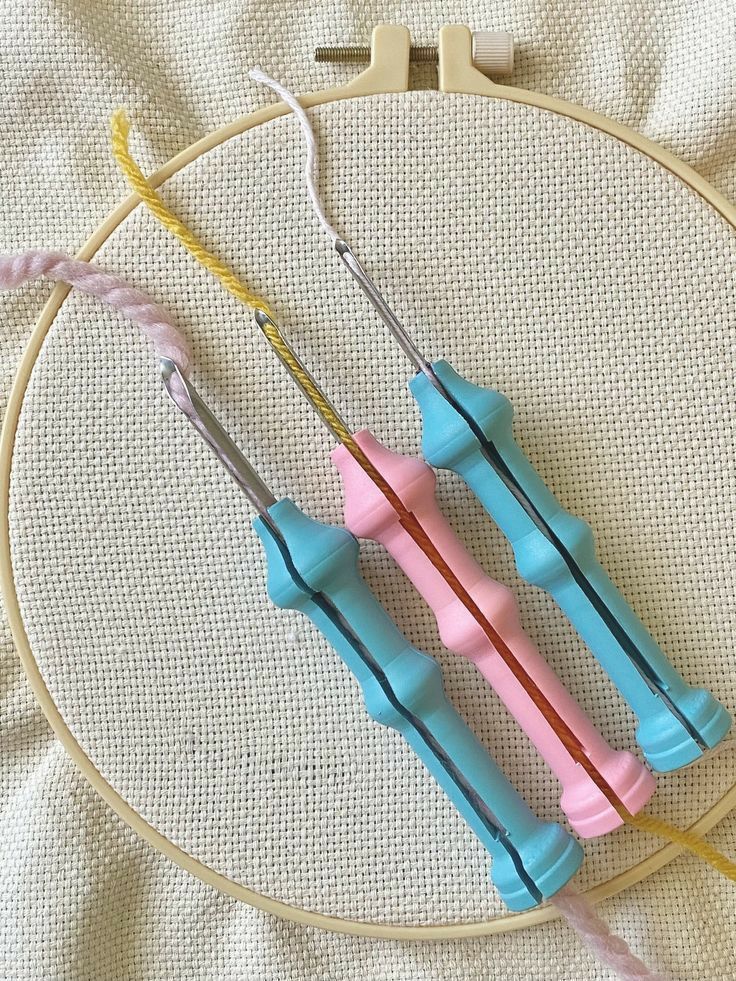 Three colorful punch needle tools placed on an embroidery hoop, showcasing pink, yellow, and white yarn for crafting projects.