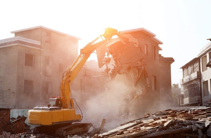 Excavator demolishing building with sunlight in background, creating dust clouds. Urban construction and demolition scene.