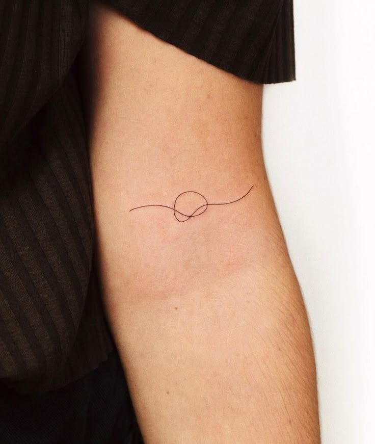 _ Minimalistic single-line tattoo of an abstract design on an arm against a striped dark fabric background. | Sky Rye Design Minimalistic single-line tattoo of an abstract design on an arm against a striped dark fabric background.