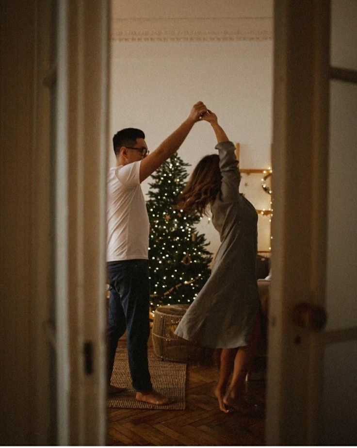 _ Couple dancing by Christmas tree with lights, in cozy home setting, viewed through a doorway. | Sky Rye Design Couple dancing by Christmas tree with lights, in cozy home setting, viewed through a doorway.