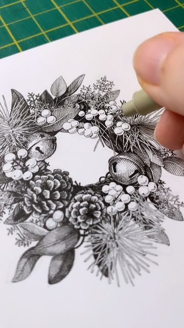 Illustration of a hand drawing a detailed wreath with pinecones and berries, using a fine-tip pen on paper. january drawing ideas