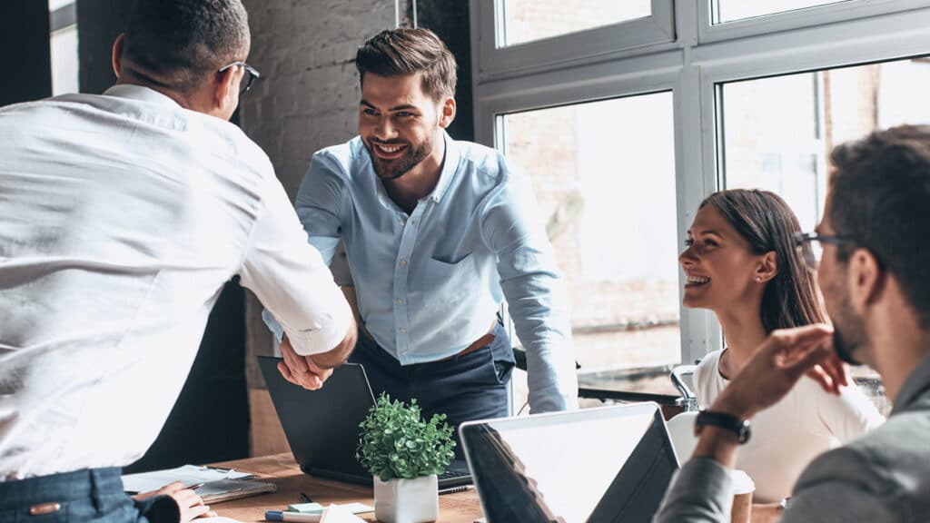 Business professionals shaking hands and smiling during a meeting in a modern office setting, fostering teamwork and collaboration.