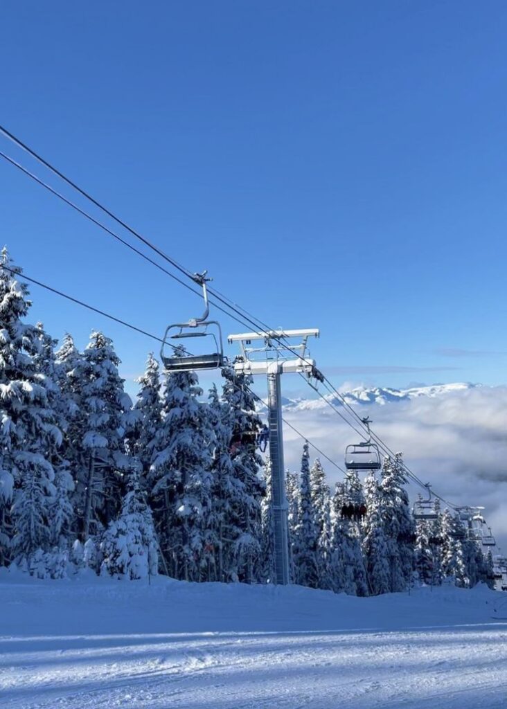 Ski lift ascending snowy mountain with snow-covered trees under a clear blue sky, capturing scenic winter landscape.