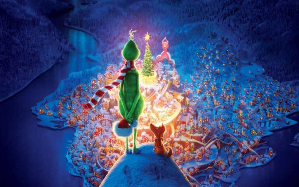 A green character and a dog overlook a festive, illuminated village from a snowy hilltop at night.