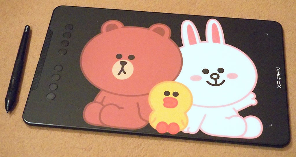 xp-pen_deco01v2_tablet-pen Digital drawing tablet with cartoon characters and stylus pen on a beige surface, ideal for creative design and illustration. | Sky Rye Design Digital drawing tablet with cartoon characters and stylus pen on a beige surface, ideal for creative design and illustration.