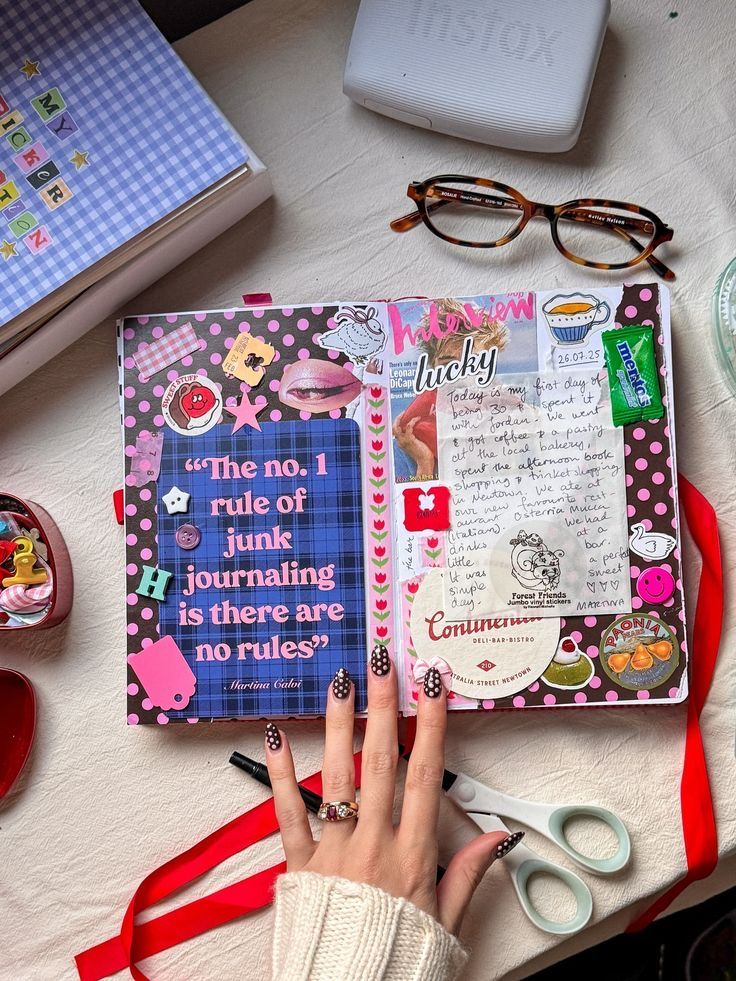 zdthzd Open junk journal on a table with various colorful stickers and embellishments. A hand with polka dot nails is visible. | Sky Rye Design Open junk journal on a table with various colorful stickers and embellishments. A hand with polka dot nails is visible.