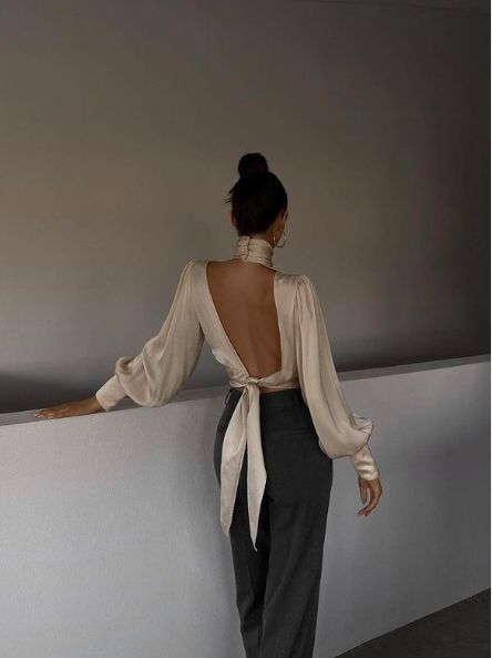 ϟ Woman wearing an open-back blouse with bow, leaning on a ledge, creating a stylish fashion statement in a minimalist setting. | Sky Rye Design Woman wearing an open-back blouse with bow, leaning on a ledge, creating a stylish fashion statement in a minimalist setting.