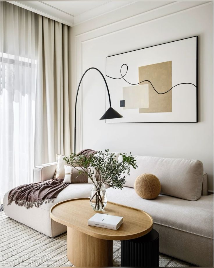 Minimalist living room with beige sofa, abstract artwork, and cozy decor. Features a wooden coffee table and elegant floor lamp.