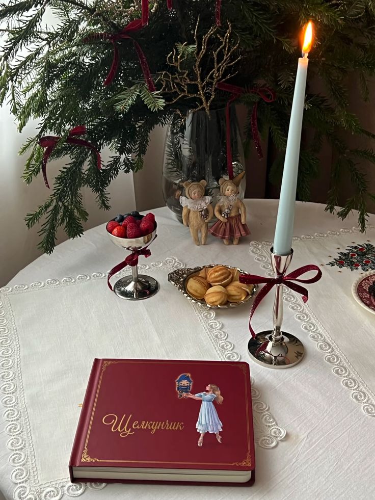 Festive table with a Nutcracker book, candle, and treats, set for a cozy holiday gathering under a decorated Christmas tree branch.
