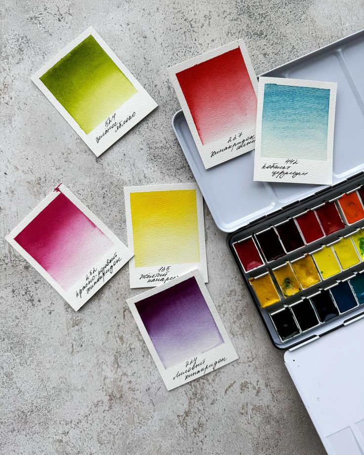 Watercolor palette with color swatches on textured background. Includes shades of green, red, blue, yellow, pink, and purple in a tin case.