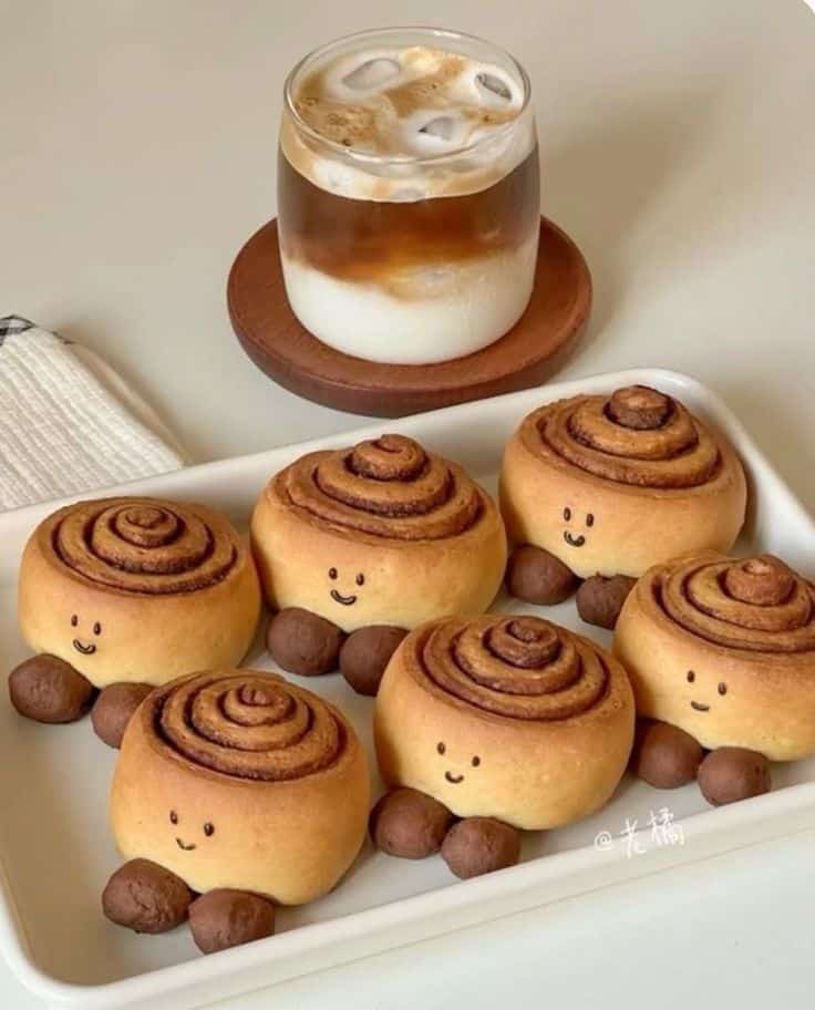 артяв Cute turtle-shaped cinnamon rolls with smiling faces and iced coffee on a wooden coaster. | Sky Rye Design Cute turtle-shaped cinnamon rolls with smiling faces and iced coffee on a wooden coaster.