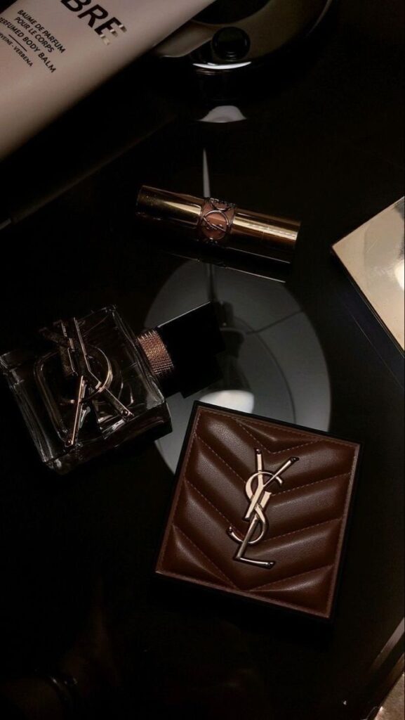 яваива Luxury YSL products on a glossy surface, featuring a perfume, lipstick, and brown quilted wallet. | Sky Rye Design Luxury YSL products on a glossy surface, featuring a perfume, lipstick, and brown quilted wallet.