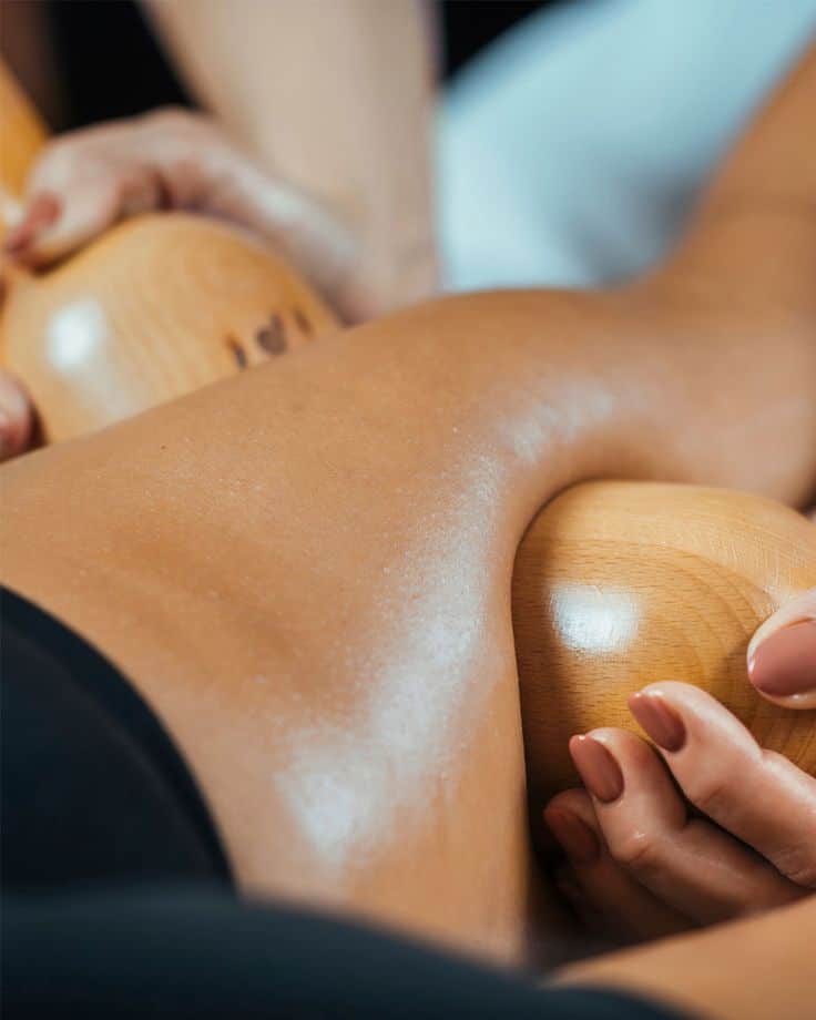 Wood therapy massage being performed on a person's leg using wooden tools, promoting relaxation and muscle tension relief.