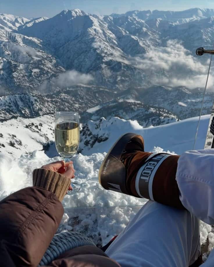 Relaxing with a glass of champagne overlooking snowy mountain peaks, enjoying winter luxury and scenic alpine views.