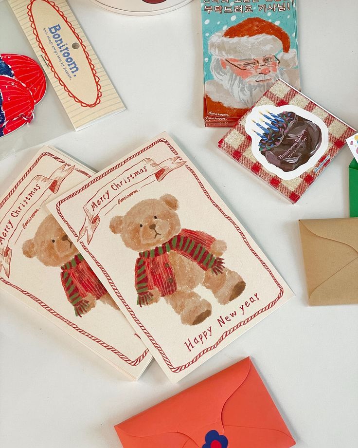 Assorted Christmas cards and envelopes featuring festive designs, including a teddy bear and Santa, laid out on a white surface.