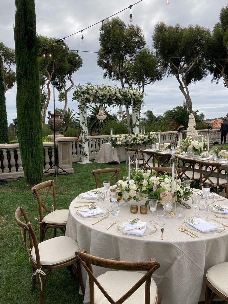 💐 Elegant outdoor wedding reception with round tables, floral centerpieces, candles, and string lights under a cloudy sky. | Sky Rye Design Elegant outdoor wedding reception with round tables, floral centerpieces, candles, and string lights under a cloudy sky.