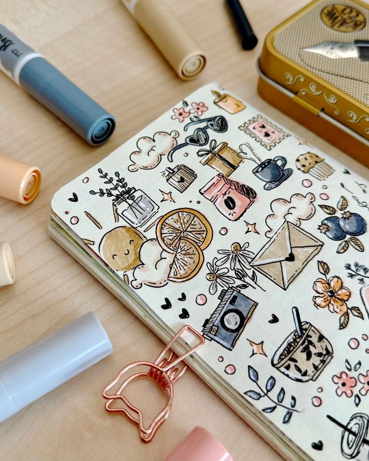 Decorative journal with doodles of plants, coffee, and mail, surrounded by pastel markers on a wooden table.