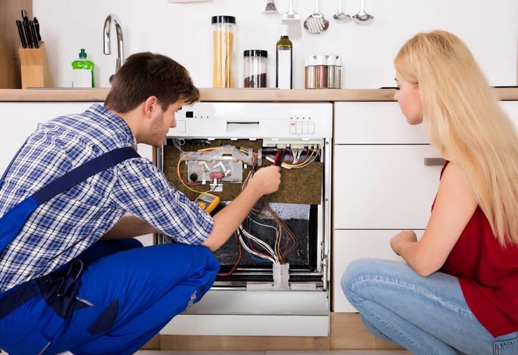 Man repairing a dishwasher while woman observes in kitchen setting.